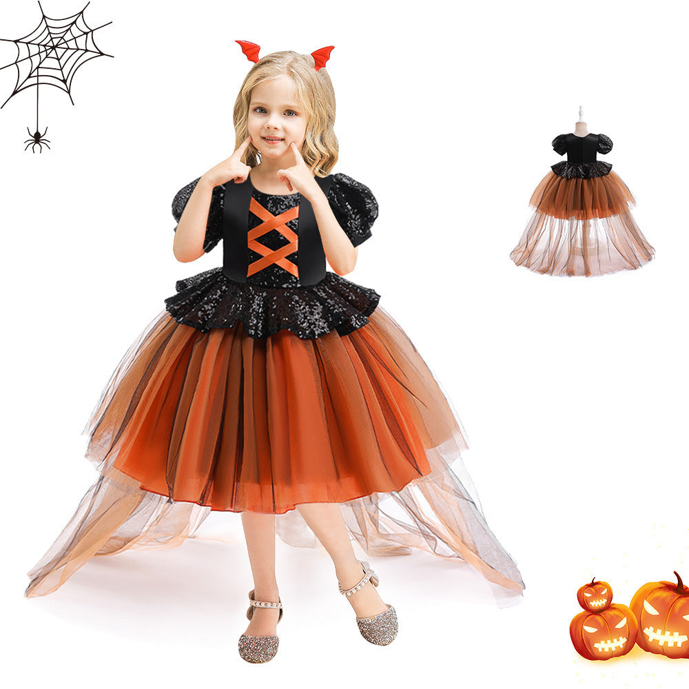 Child wearing a Halloween-themed dress with black and orange colors, standing next to pumpkins and a spider web.