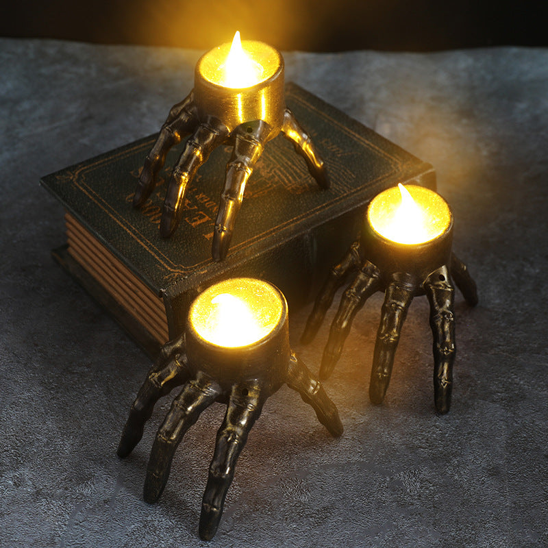 Decorative candle holders shaped like skeleton hands on a book with a dark background