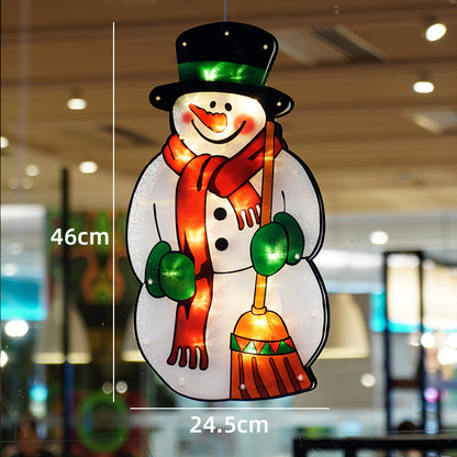 Decorative snowman ornament with a broom, wearing a green hat and red scarf, against a blurred indoor background.