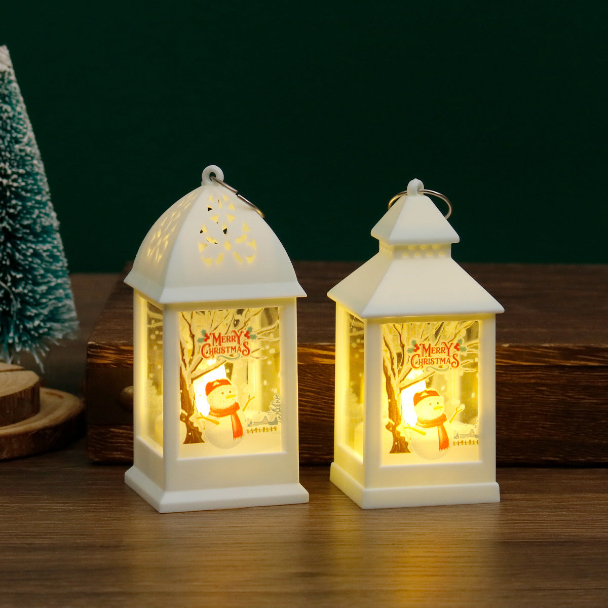 Two illuminated Christmas lanterns with snowman designs on a wooden surface.