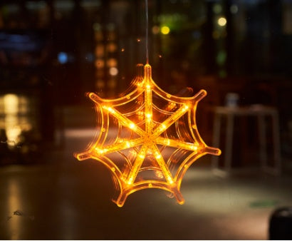 Spider web-shaped light decoration with glowing orange lights against a blurred background