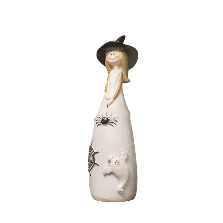Decorative figurine of a witch with a black hat, white dress, and cat, standing on a wooden surface with a blurred background.
