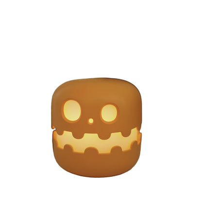 Ceramic skull-shaped lantern with glowing interior on a surface, blurred candles in the background
