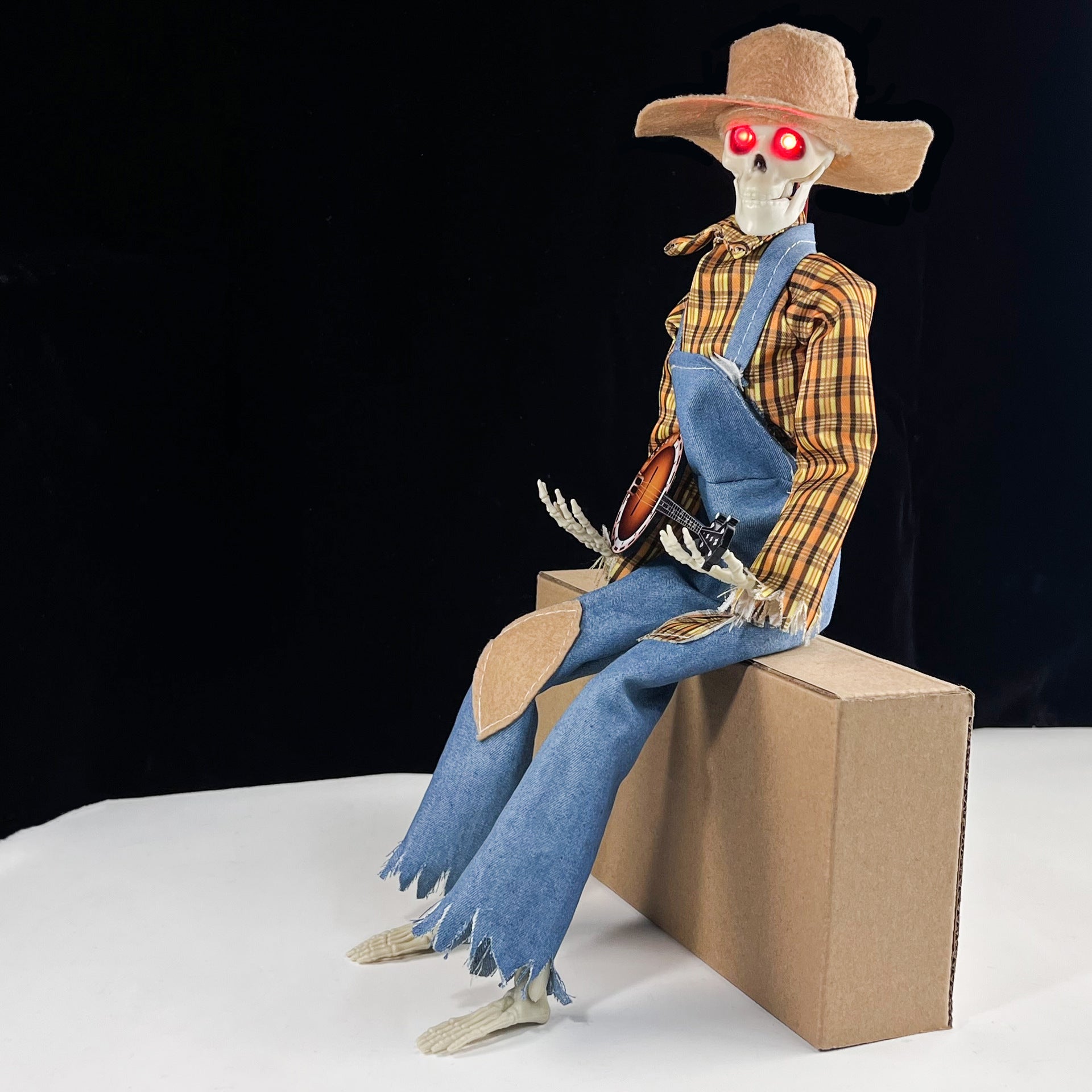 Skeleton figure in a cowboy outfit with a guitar, sitting on a box against a black background.
